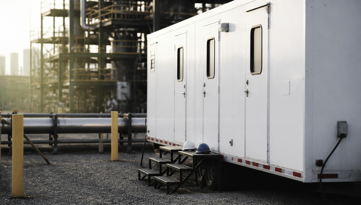 Climate-controlled break trailer staged on gravel beside an industrial plant at first light